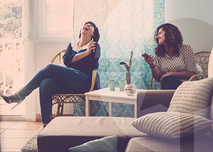 Two women sit at home laughing over something funny on a mobile phone